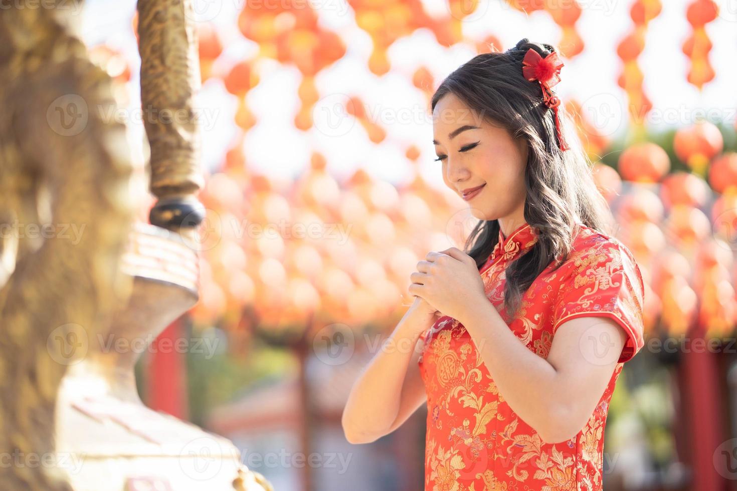 hermosa mujer asiática con traje tradicional cheongsam qipao rezando por la mejor bendición y buena suerte en el templo budista chino. emoción sonrisa foto