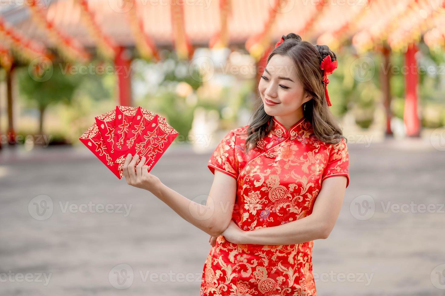 Happy Chinese new year. Beautiful lady wearing traditional cheongsam qipao dress looking confident holding ang pao, red envelopes in Chinese Buddhist temple. Chinese text means great luck photo