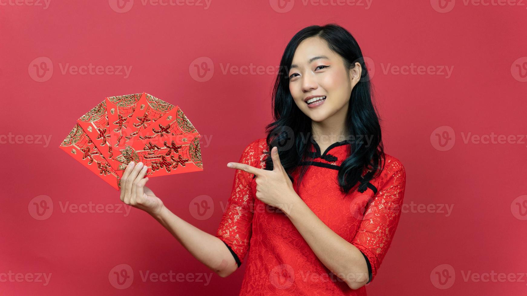 Beautiful woman with red cheongsam or qipao hand pointing to blessing fortune card isolated on red background. Chinese text means great luck great profit photo