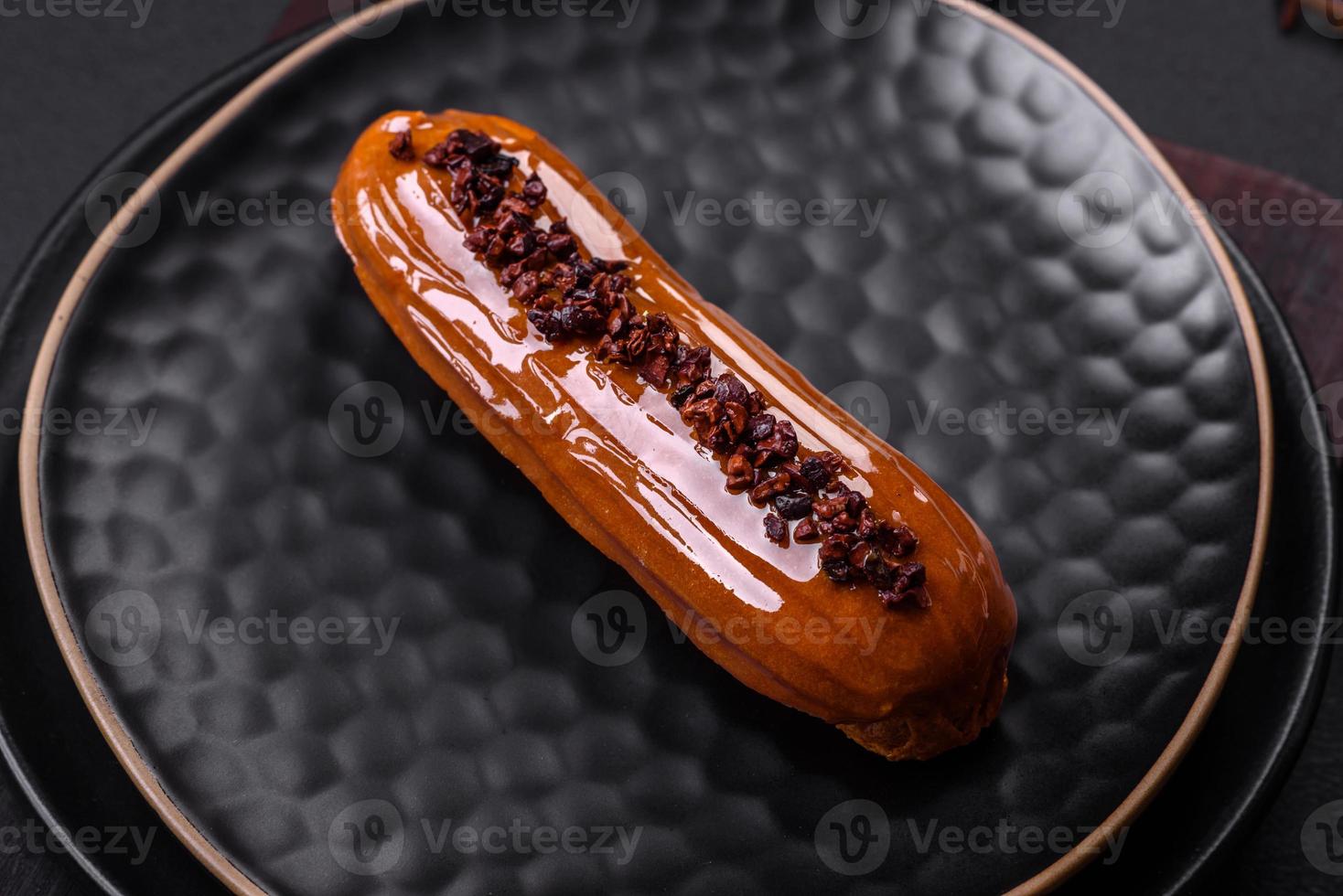 Delicious fresh eclair with chocolate cream on a black ceramic plate photo