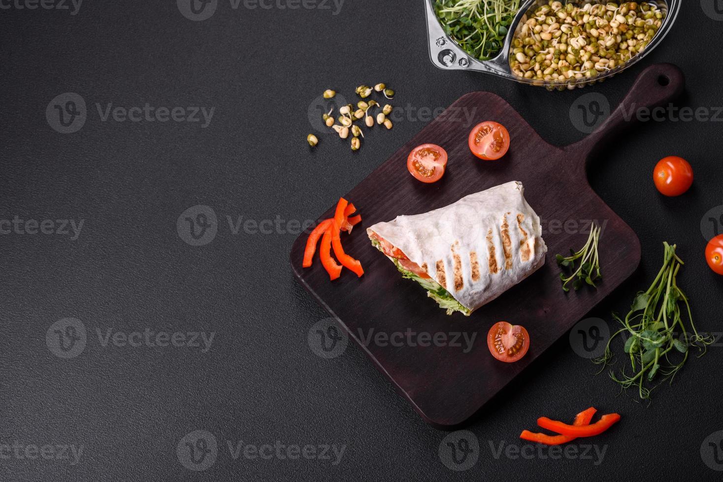 Delicious fresh shawarma with tomatoes, peppers, cucumber on a dark concrete background photo