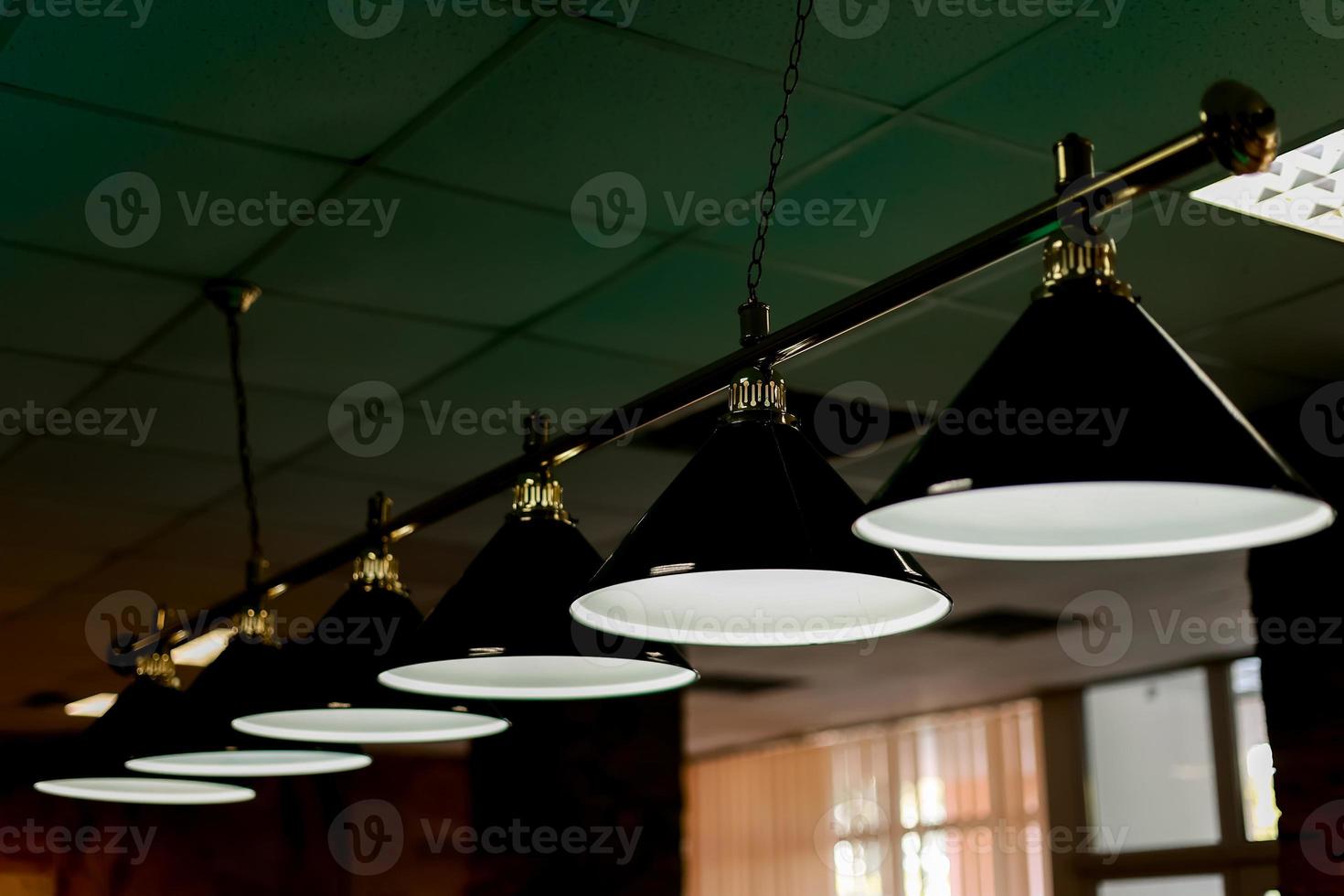 fila de lámparas de billar encima de la mesa brillan en la oscuridad en el pub. fondo abstracto de juegos de azar y recreación. foto