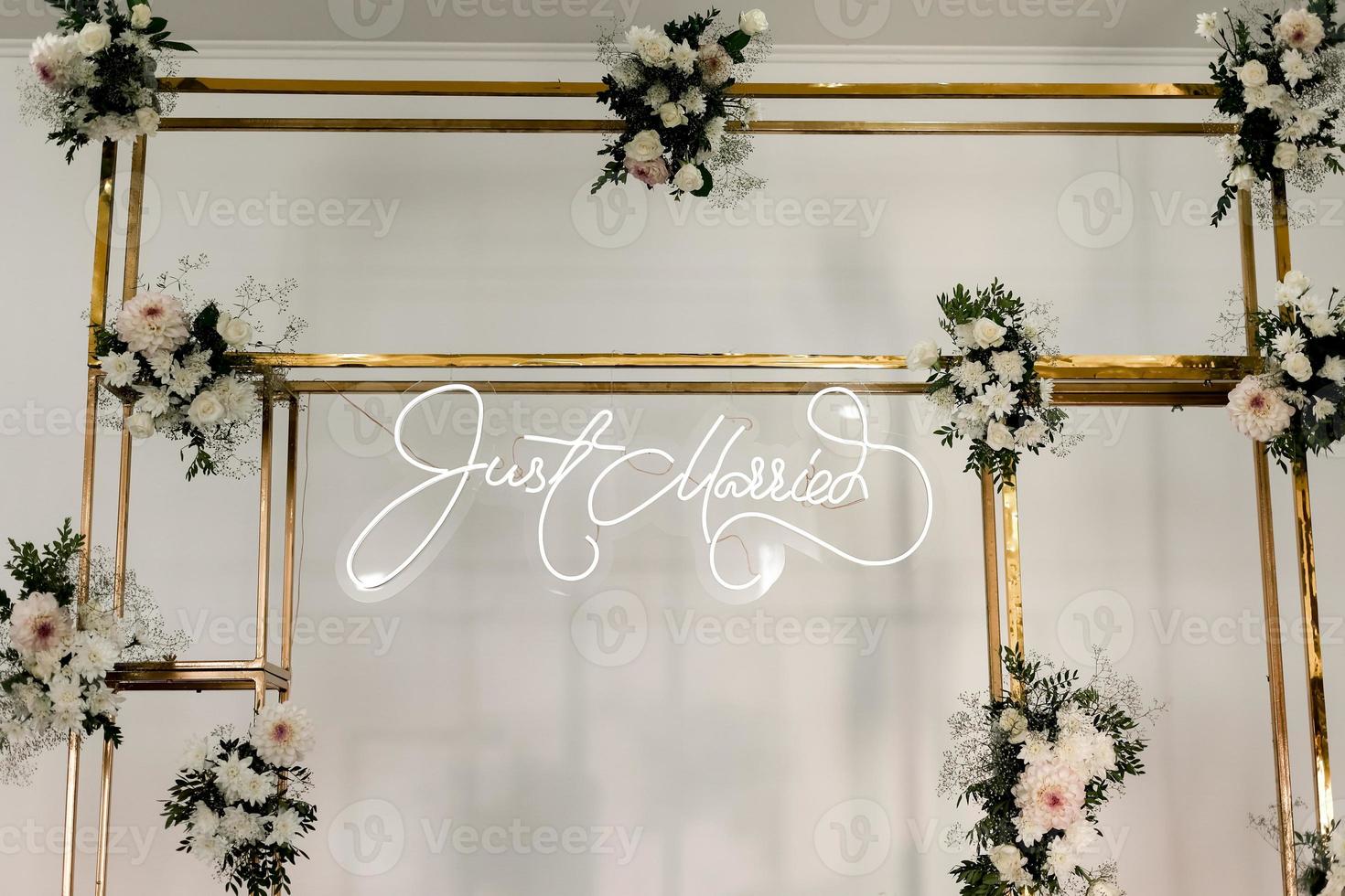 wedding rectangular metal gold arch design with fresh white flowers and greens on a white wall background. Festive decoration photo zone indoors