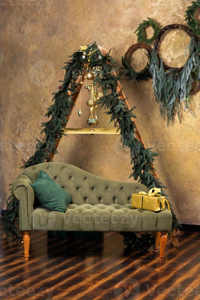 Christmas composition with decoration, christmas tree branch, stylish green classic sofa, gift boxes and accessories in cozy home decor. Happy xmas and New Year holiday concept. Vertical photo