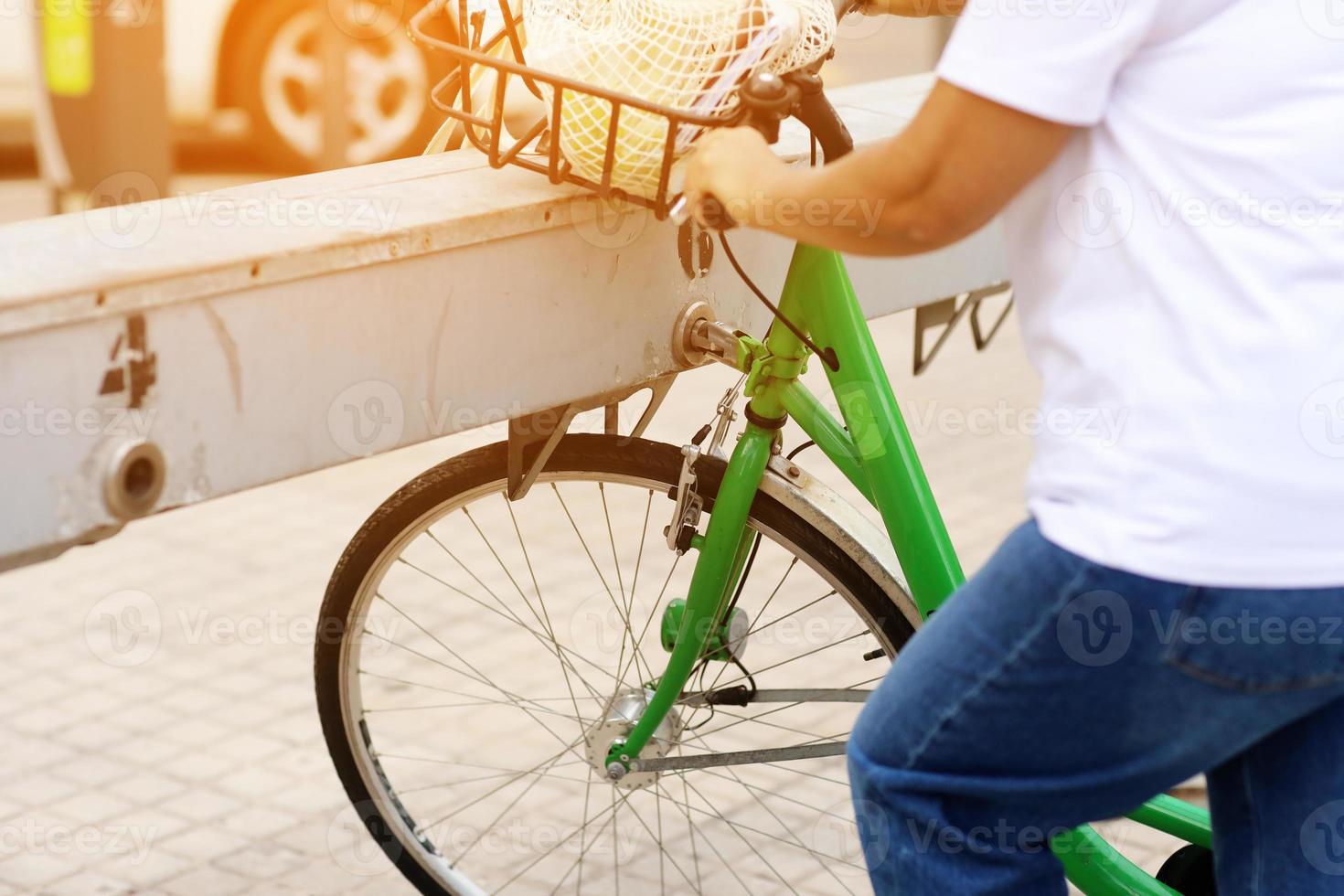 cropped photo of unrecognizable woman in white t-shirt and jeans is picking up a green bike at a bike rental station in the city. urban lifestyle concept on summer day