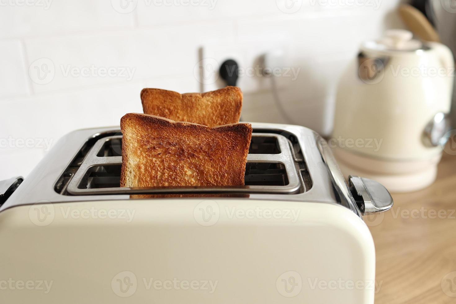 Modern white toaster and roasted bread slices toasts inside on wooden table in kitchen photo