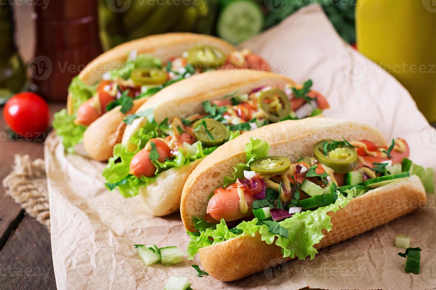 perrito caliente con pimientos jalapeños, tomate, pepino y lechuga sobre fondo de madera foto