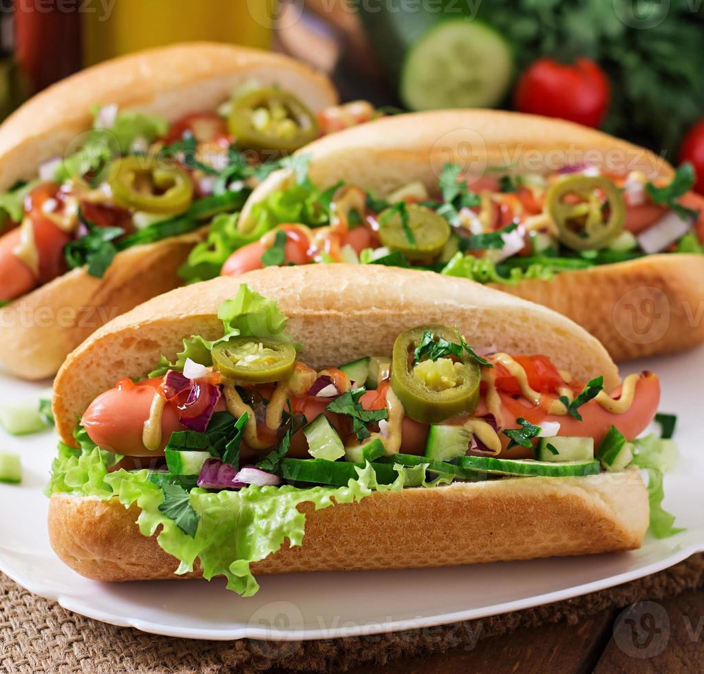 Hot dog with jalapeno peppers, tomato, cucumber and lettuce on wooden background photo