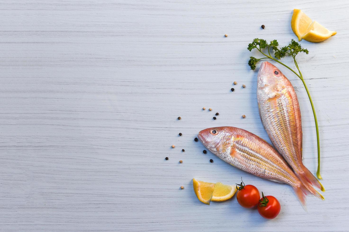 Fresh raw fish seafood with herbs and spices with lemon parsley tomato pepper seed on white wood background photo