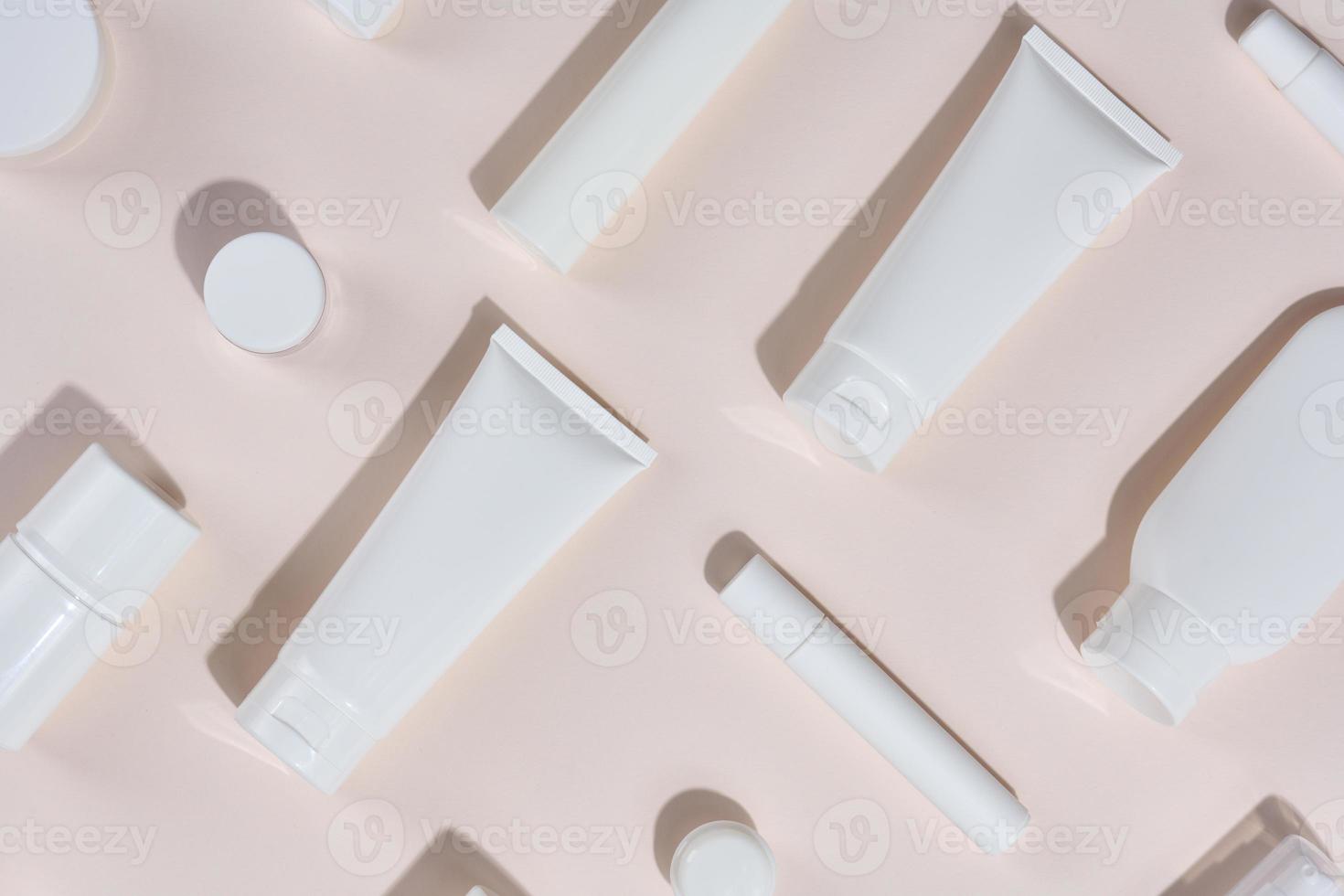 White plastic tubes, jars and other form of packaging for cosmetics on a beige background, top view. photo