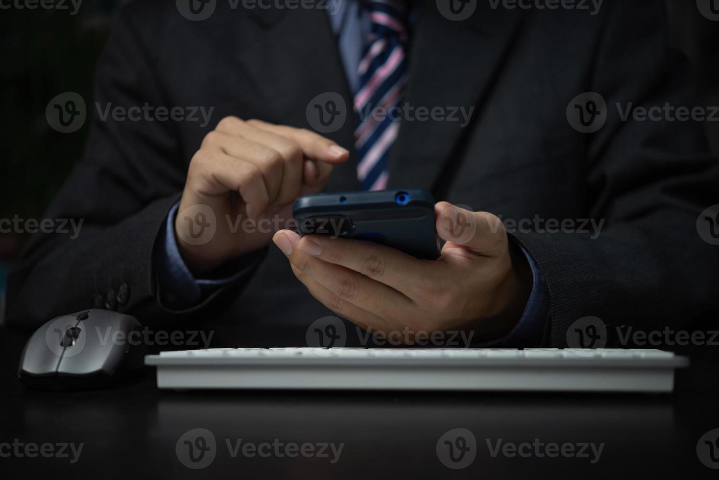 Business man holding mobile smartphone and keyboard computer on desk. photo