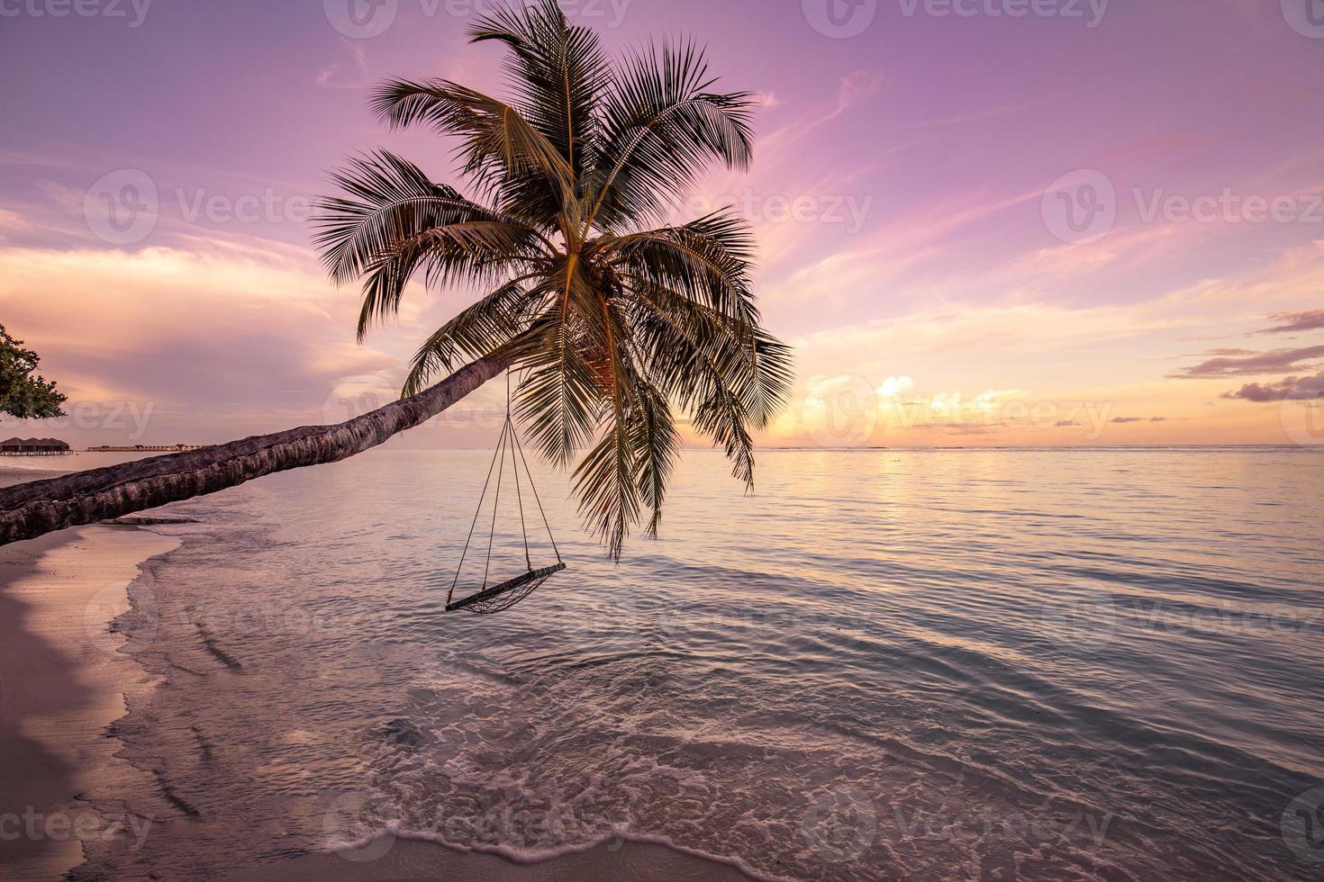 A view of a beach with palm trees and swing at sunset. Unique landscape, serene peaceful paradise. Perfect romantic beach sunset scenery, calm sea, colorful sky. Beautiful tropical nature pattern photo