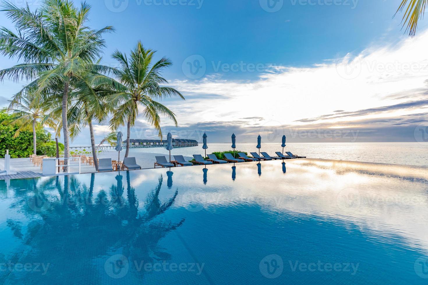 complejo de playa tropical con tumbonas y sombrillas y palmeras de coco. hermosa mañana tranquila, piscina infinita cerca del mar y la playa, reflejo del cielo. vacaciones tropicales tranquilas de lujo foto