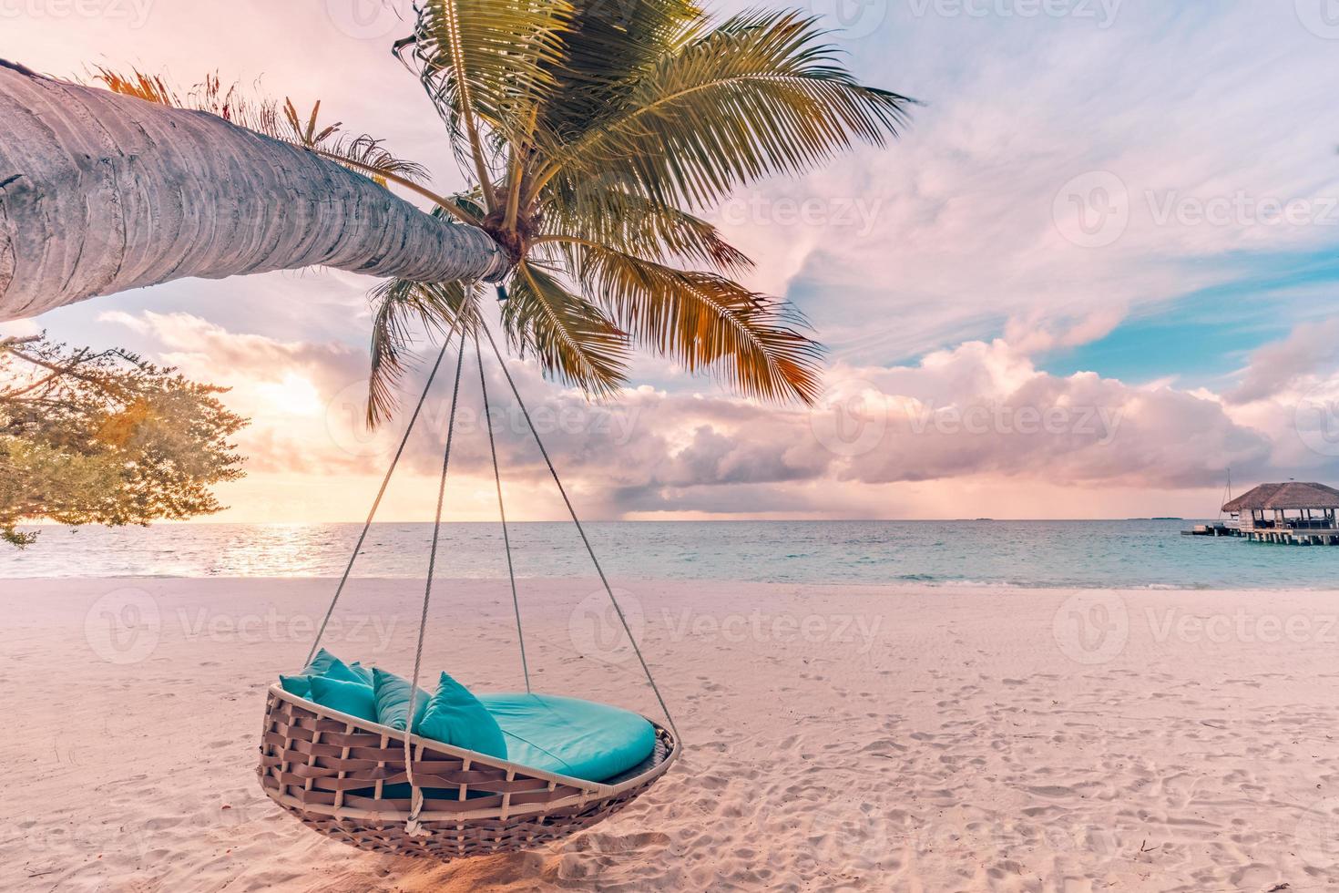 Tropical beach sunset landscape with beach swing or hammock and sunset sky white sand and calm sea for beach banner. Perfect beach scene vacation and summer holiday concept. Boost up color process photo