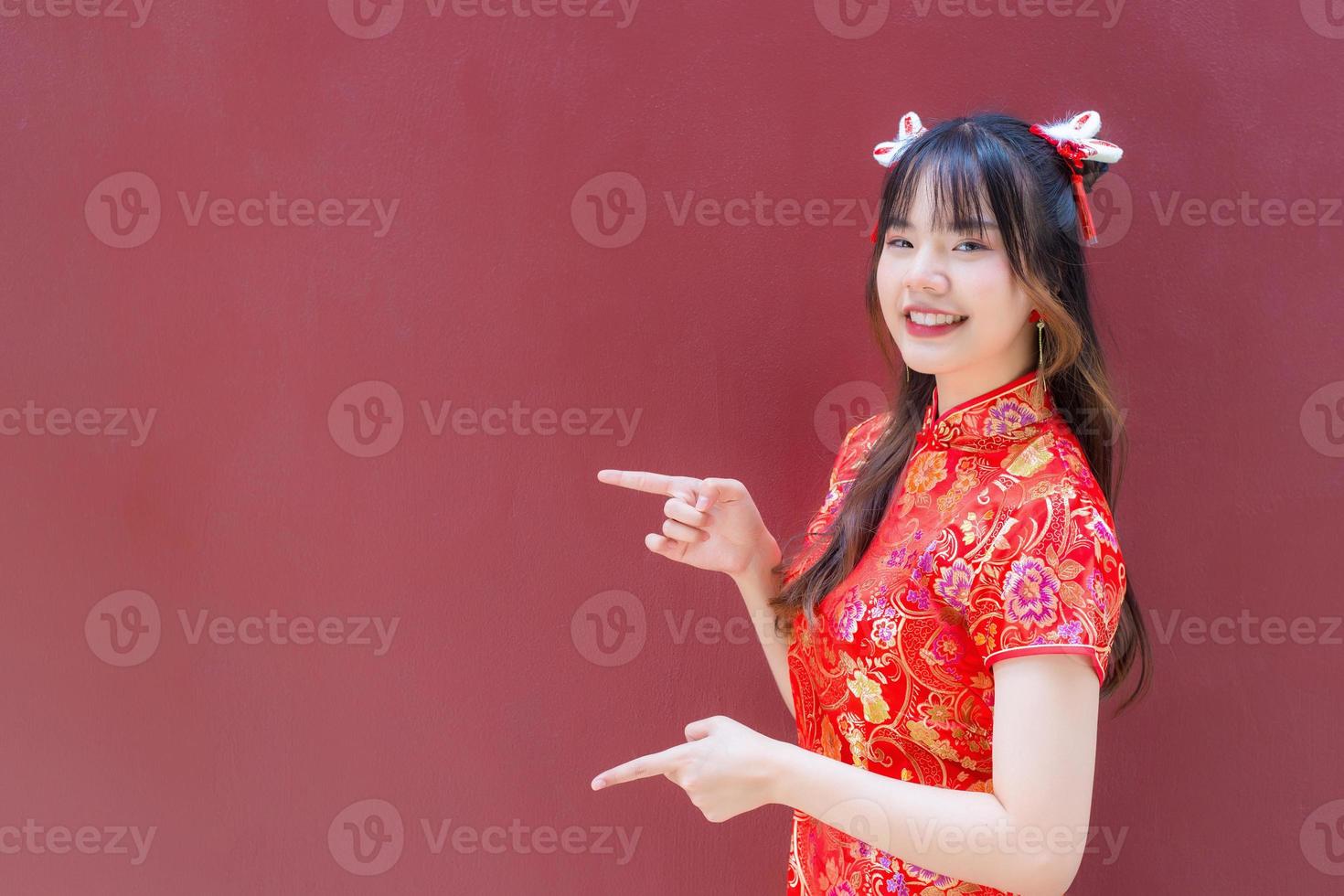 Cute Asian girl with long hair who wears a red Cheongsam dress in Chinese new year theme while she shows her hand to present something on a red background. photo