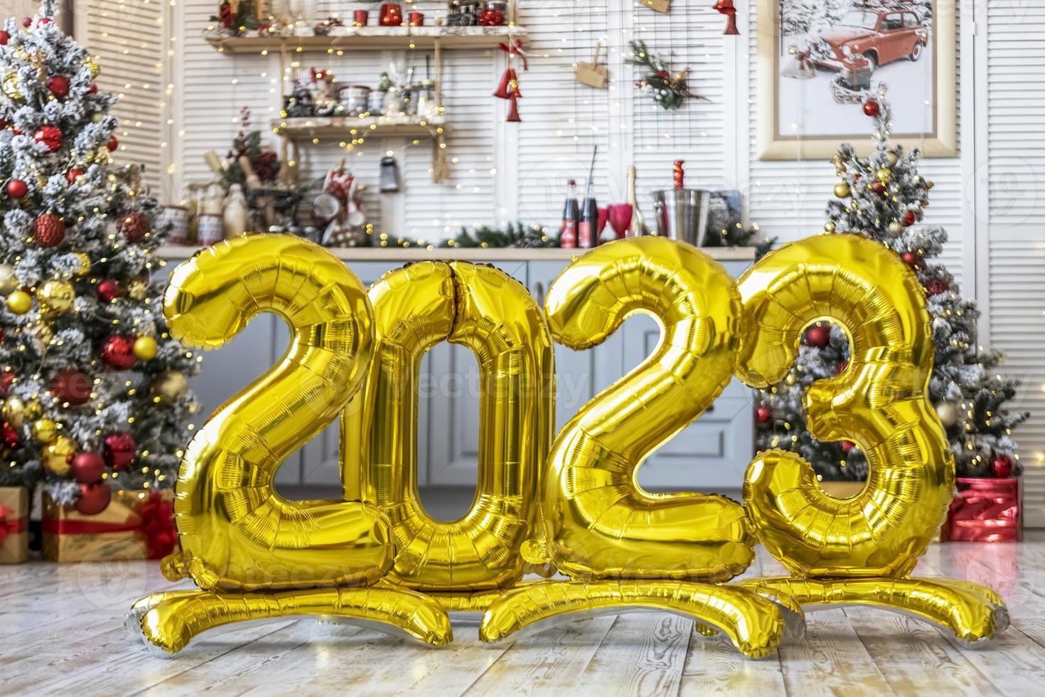 A golden balls in the form of numbers 2023 on the background of a Christmas tree. People are celebrating the new year, waiting, anticipating. The concept of the new year and celebration. photo