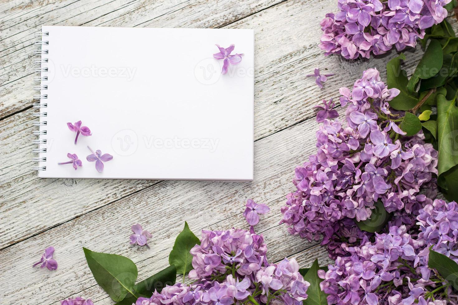 Bloc de notas limpio con flores lilas de primavera sobre fondo blanco de madera foto