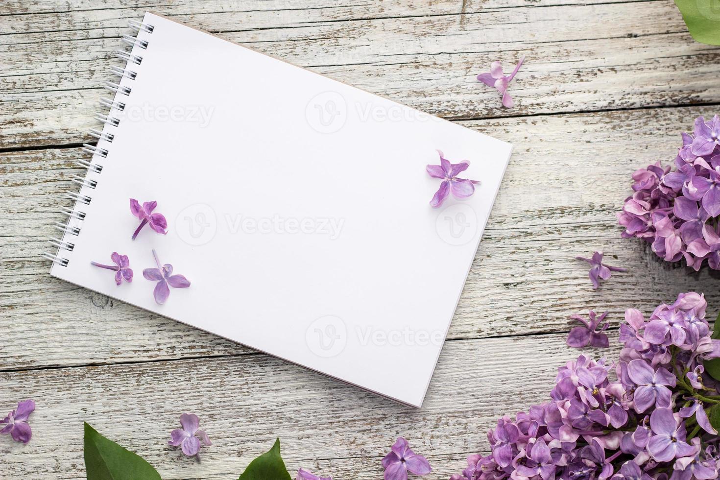 Clean notepad with spring lilac flowers on white wooden background photo