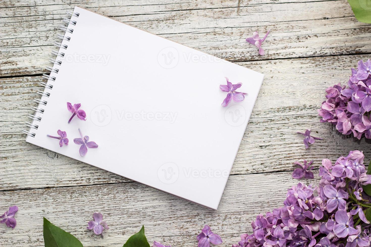 Bloc de notas limpio con flores lilas de primavera sobre fondo blanco de madera foto