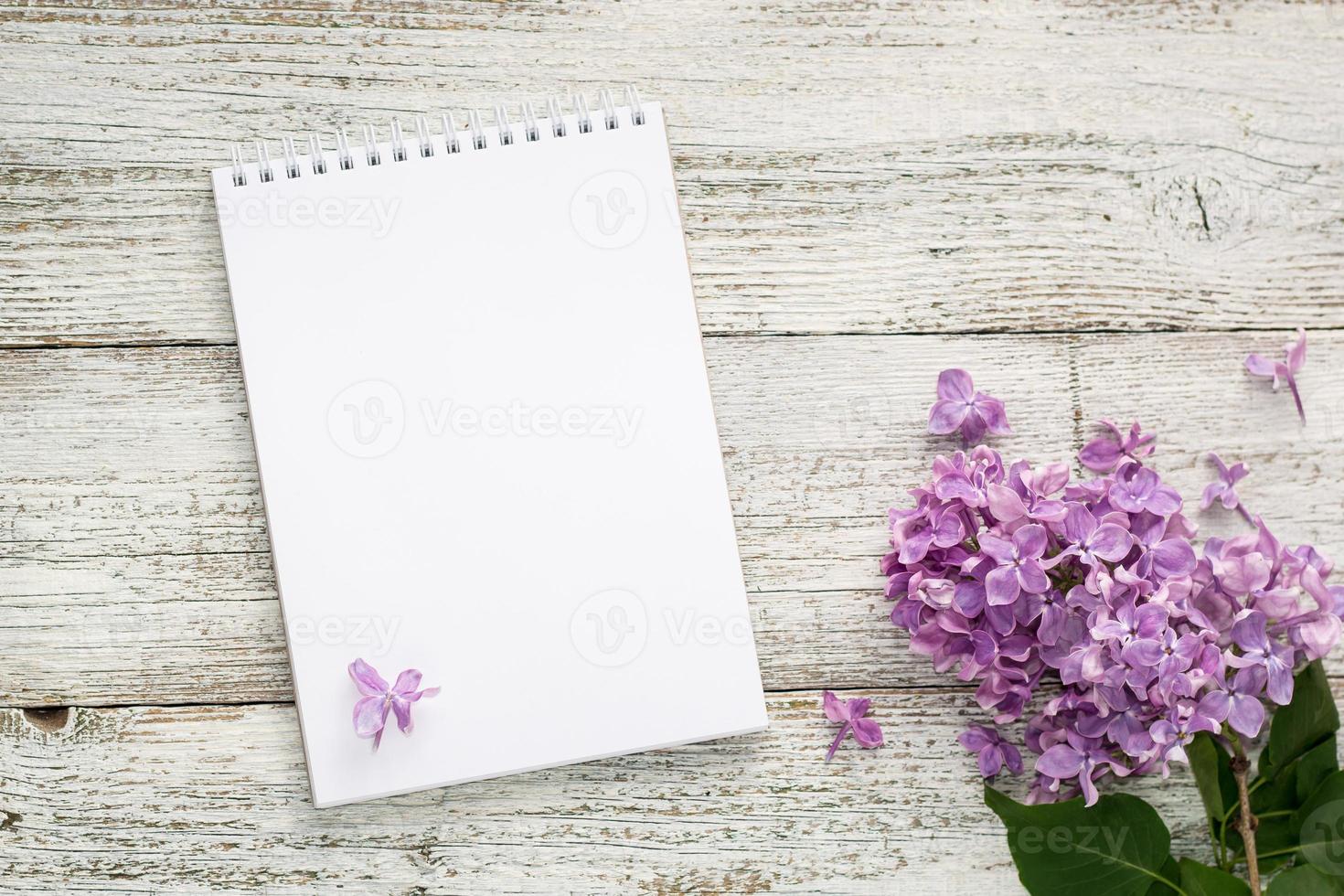 Bloc de notas limpio con flores lilas de primavera sobre fondo blanco de madera foto