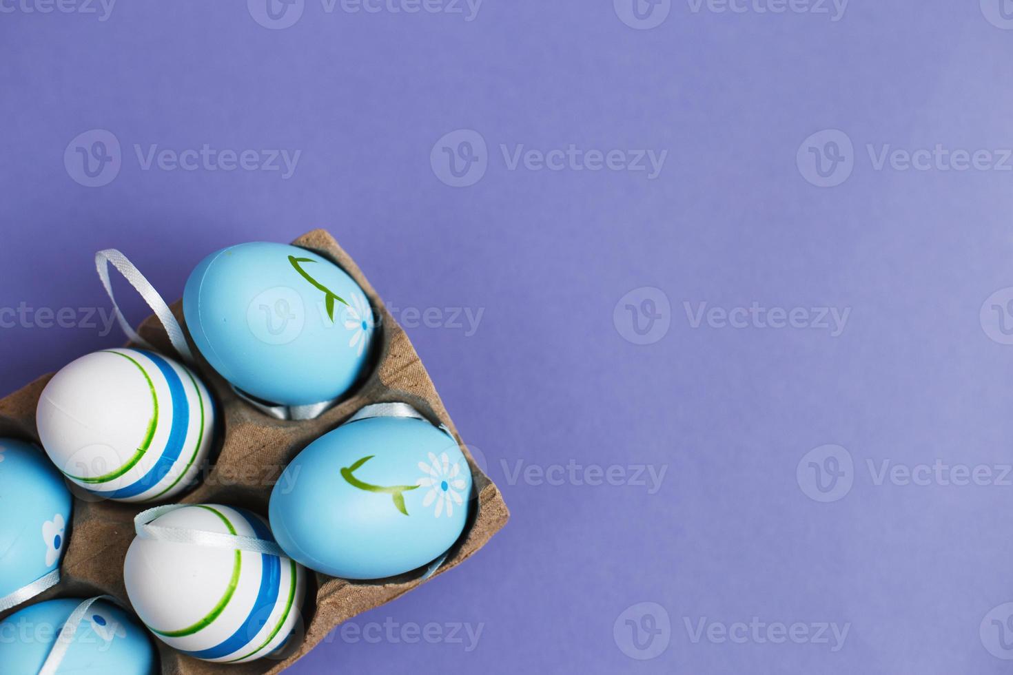 top view easter colorful handmade painted blue eggs in a box on purple background photo