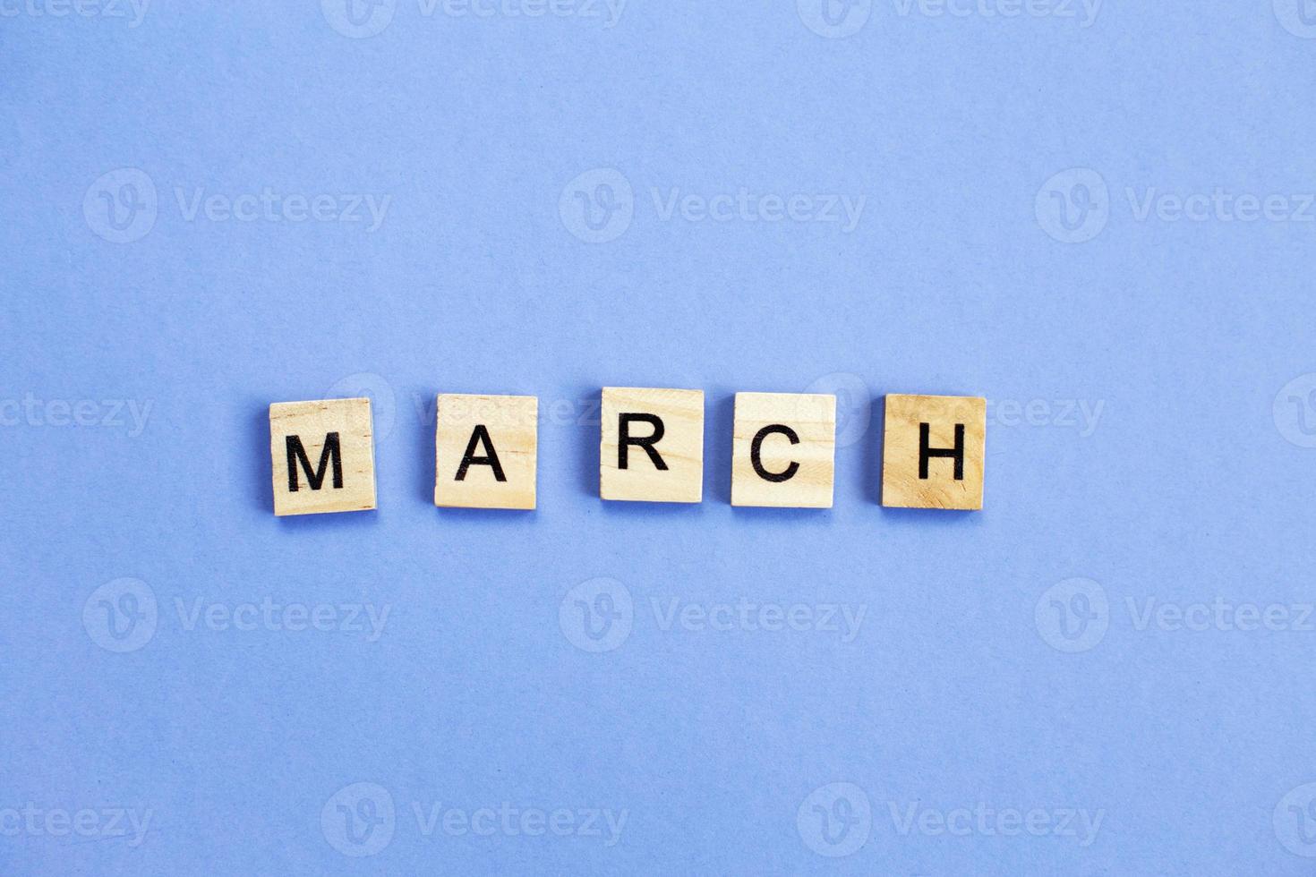 inscription March made by wooden cubes on a veri peri purple background. photo