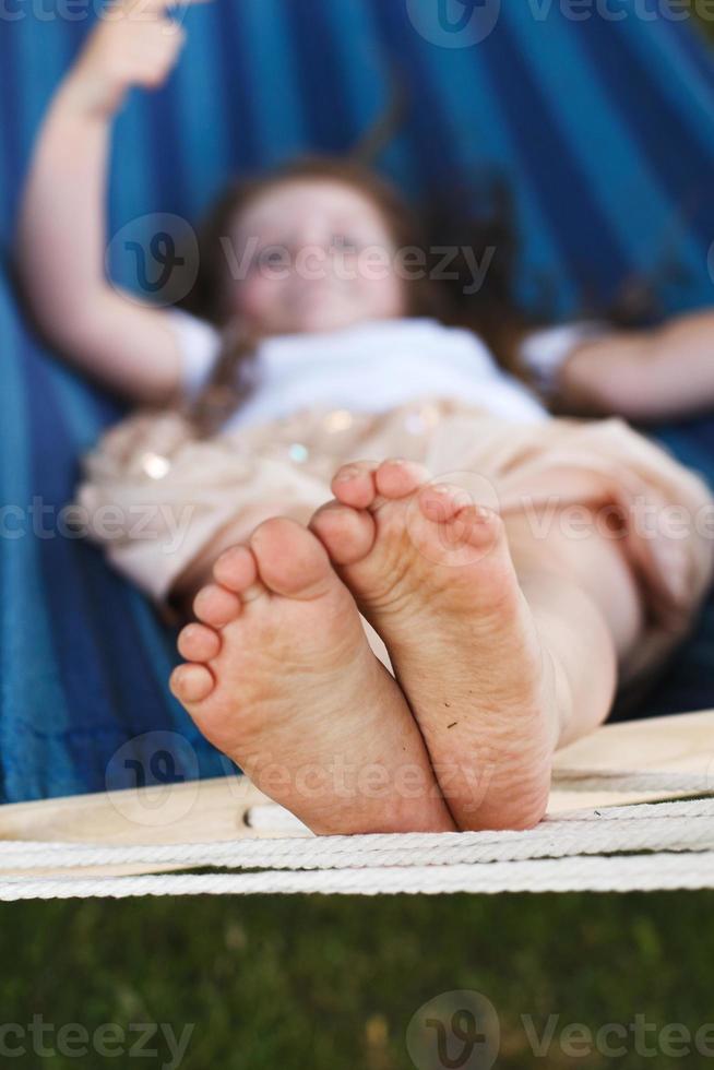 closeup of little girl's feet relaxing in the blue hammock during her summer vacation in back yard photo