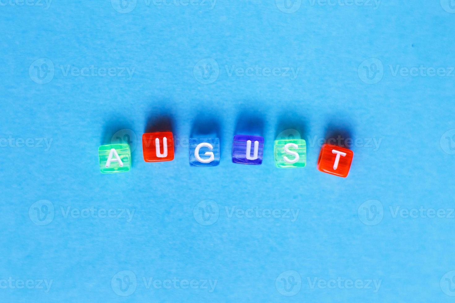 inscripción agosto hecha por cubos de plástico multicolores sobre un fondo azul. foto