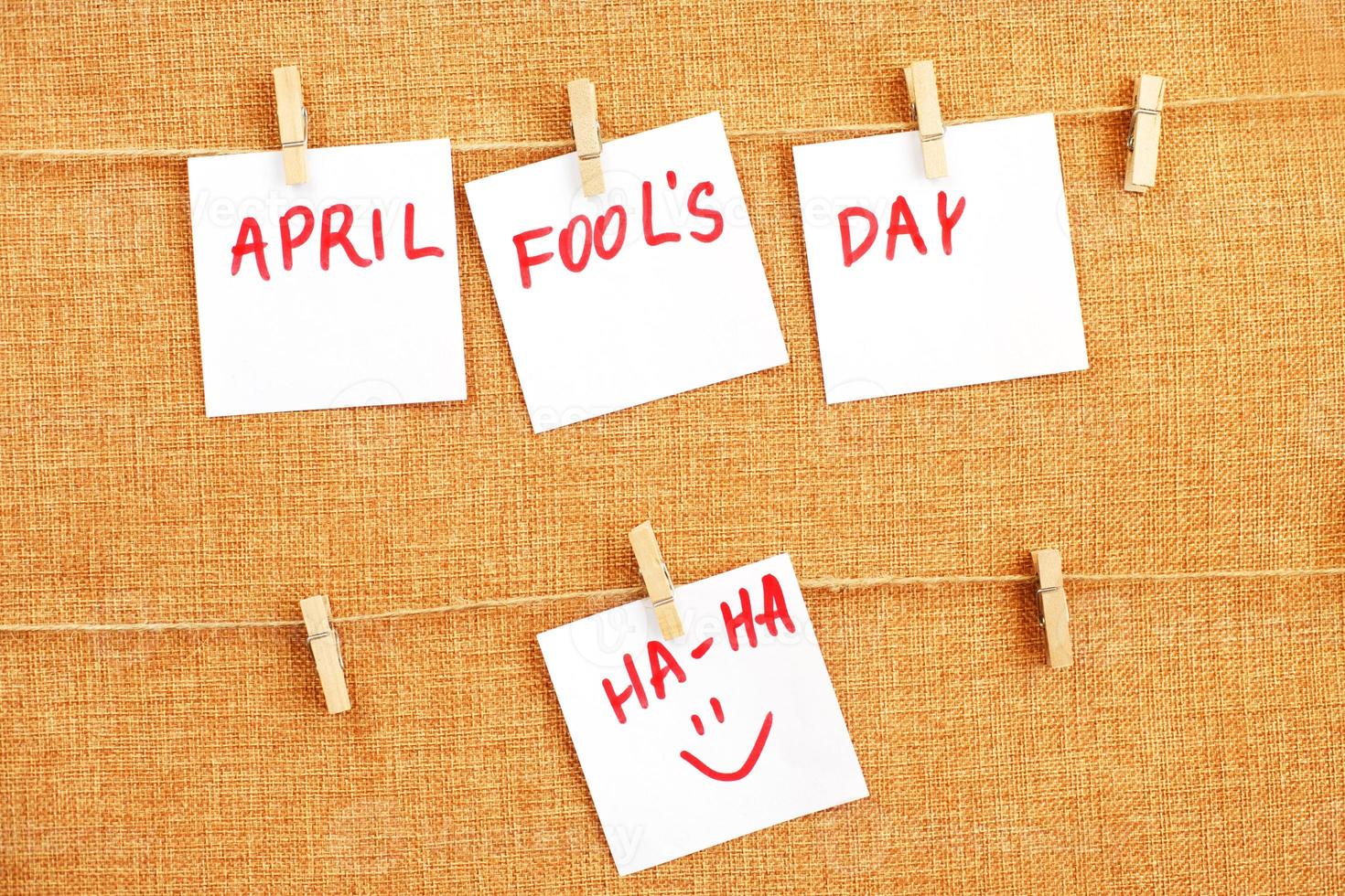 stickers with smiley hanging on the pin and inscription april fools day on brown textile background photo