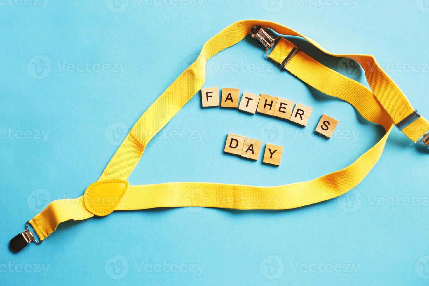 happy father's day lettering made by wooden cubes on a blue background with a yellow suspenders photo