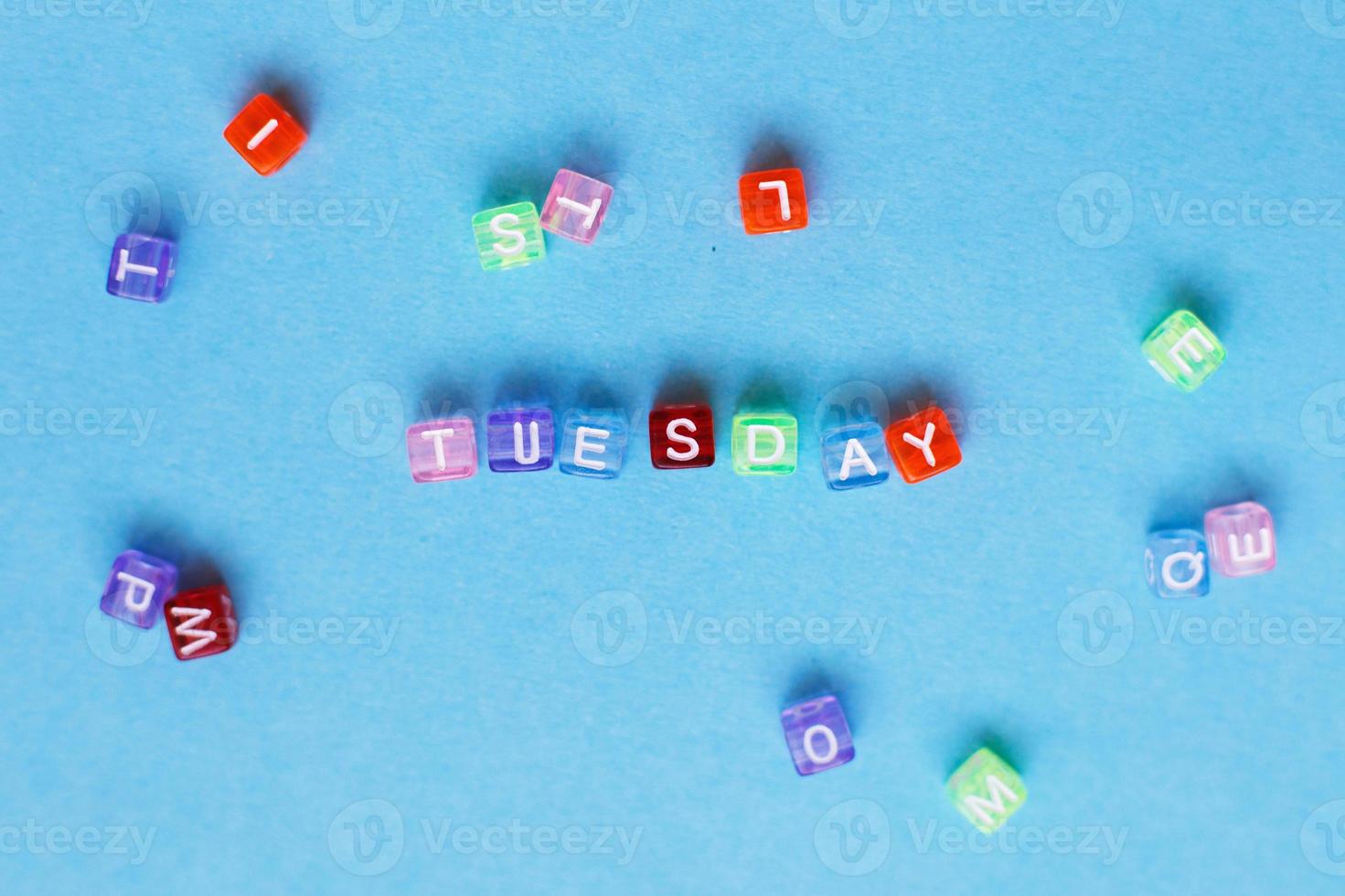 inscription Tuesday made by multicolor plastic cubes on a blue background. photo