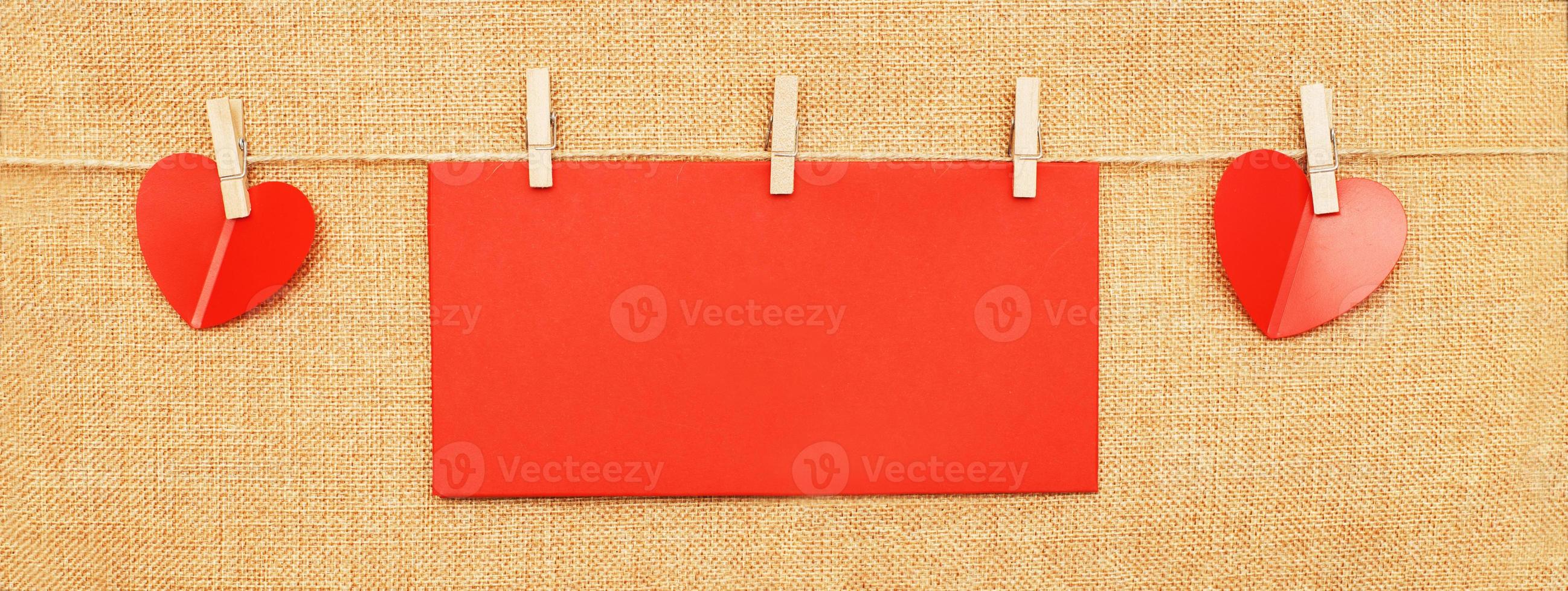 red hearts with paper note for text on clothes pin on brown textile background photo