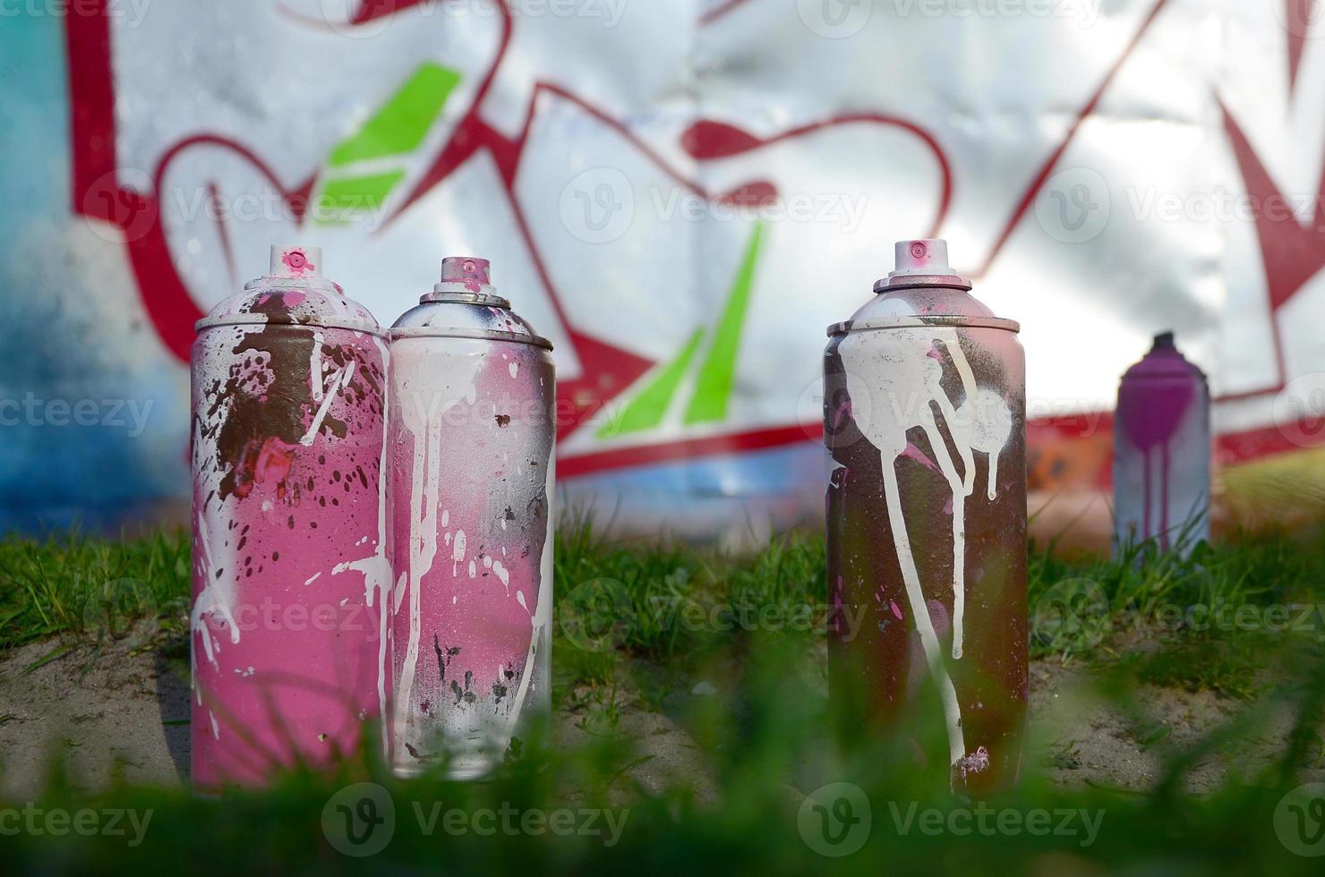 A few used paint cans lie on the ground near the wall with a beautiful graffiti painting. Street art and vandalism concept photo