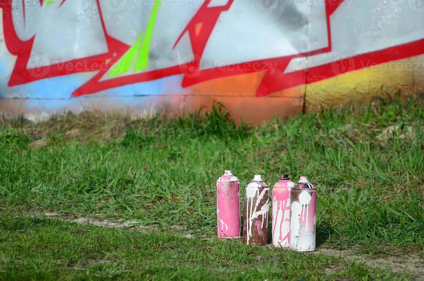 A few used paint cans lie on the ground near the wall with a beautiful graffiti painting. Street art and vandalism concept photo