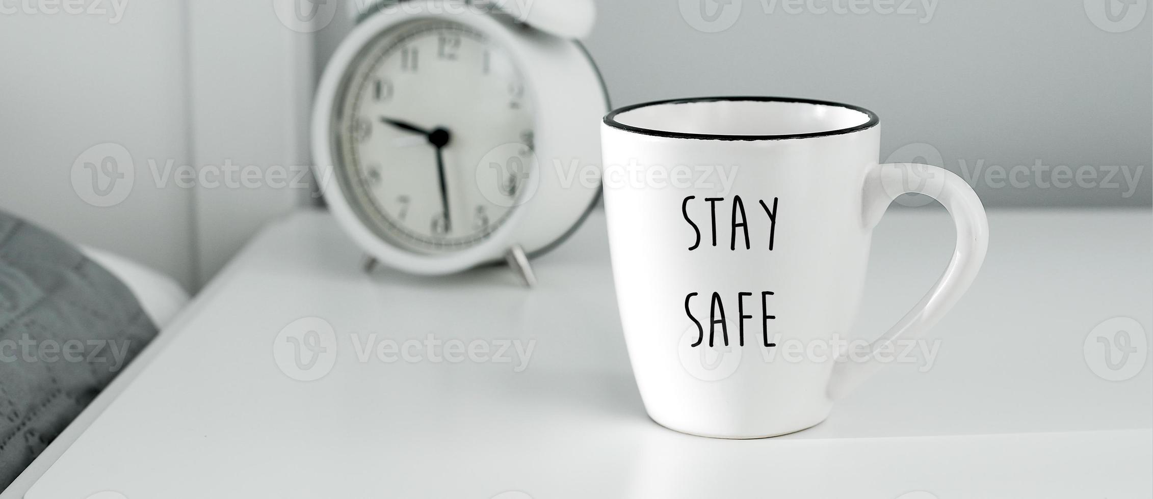 Morning home routine. White cup of coffee and alarm clock on bedside table. Stay home, stay safe, self isilation, quarantine concept. Banner image for website photo