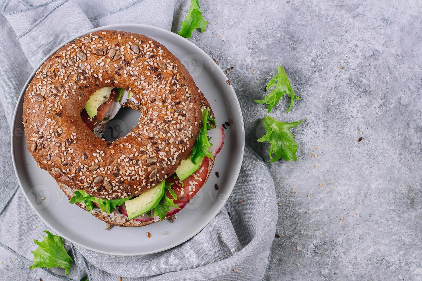 Veggie Bagels with avocado, tomatos, radish and green leaves on concrete table. Healthy lunch. photo