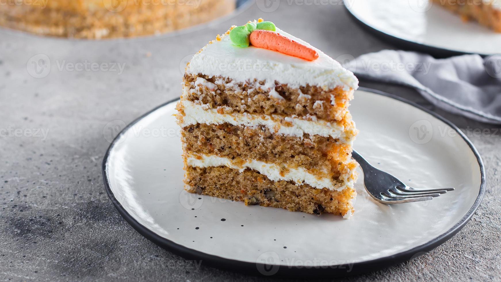 Slice of homemade carrot cake with cream cheese frosting on plate on gray stone table background. photo