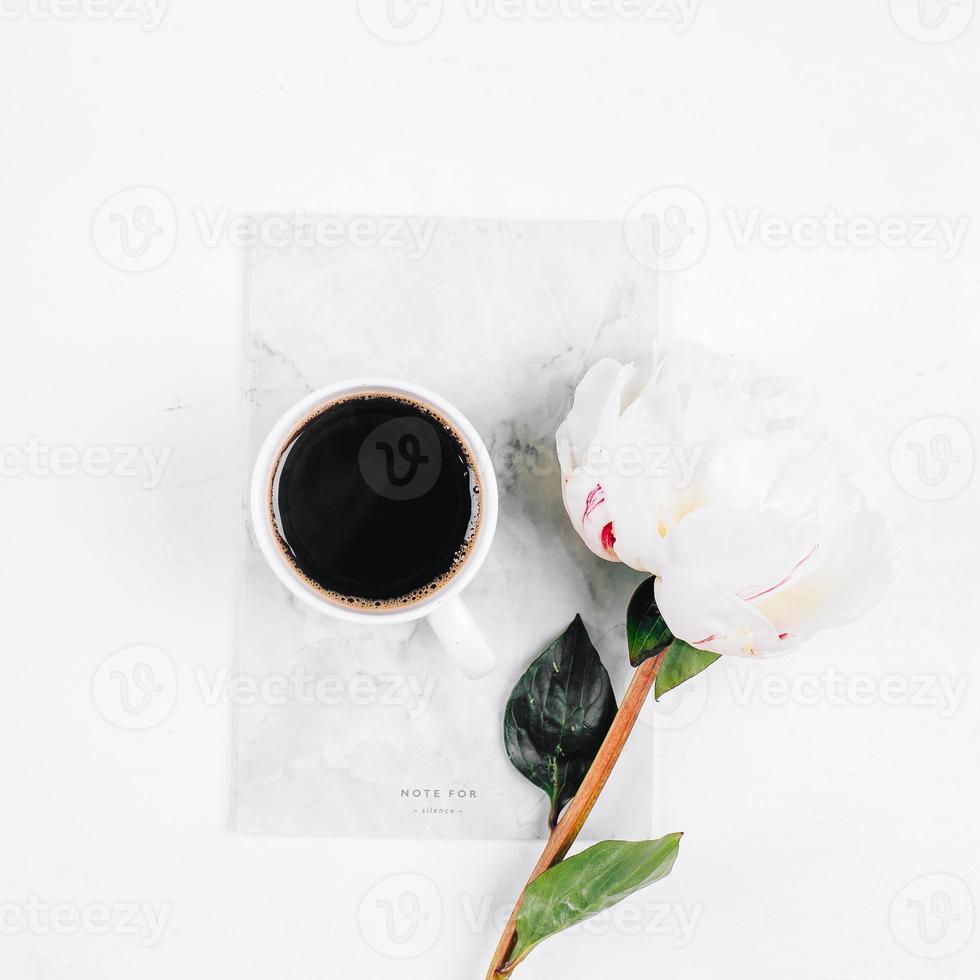 Coffee mug, notebook and white peony flowers on pink table background. Cozy, still life, minimal concept. Top view, flat lay, copy space photo