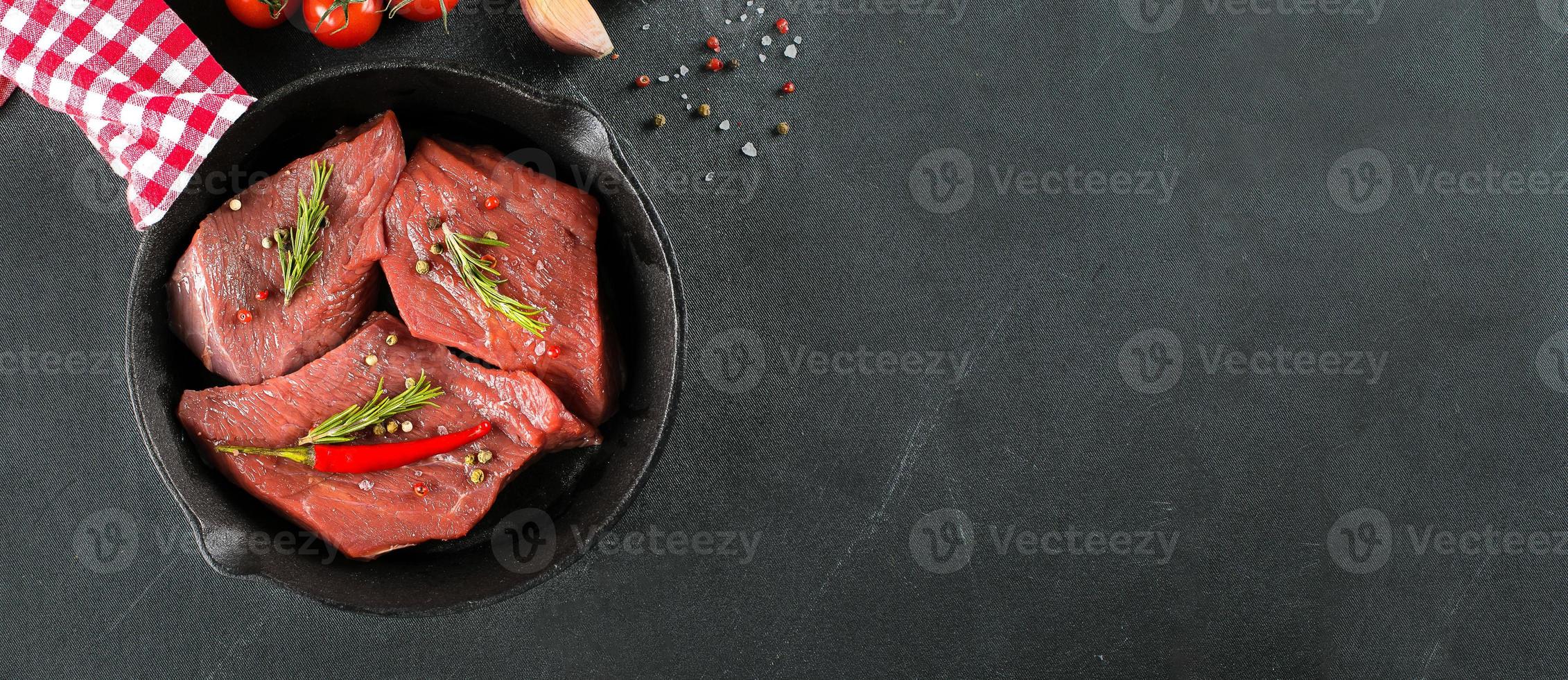 Raw meat. Raw beef steak on a black board with herbs and spices. Top view. Banner for design photo
