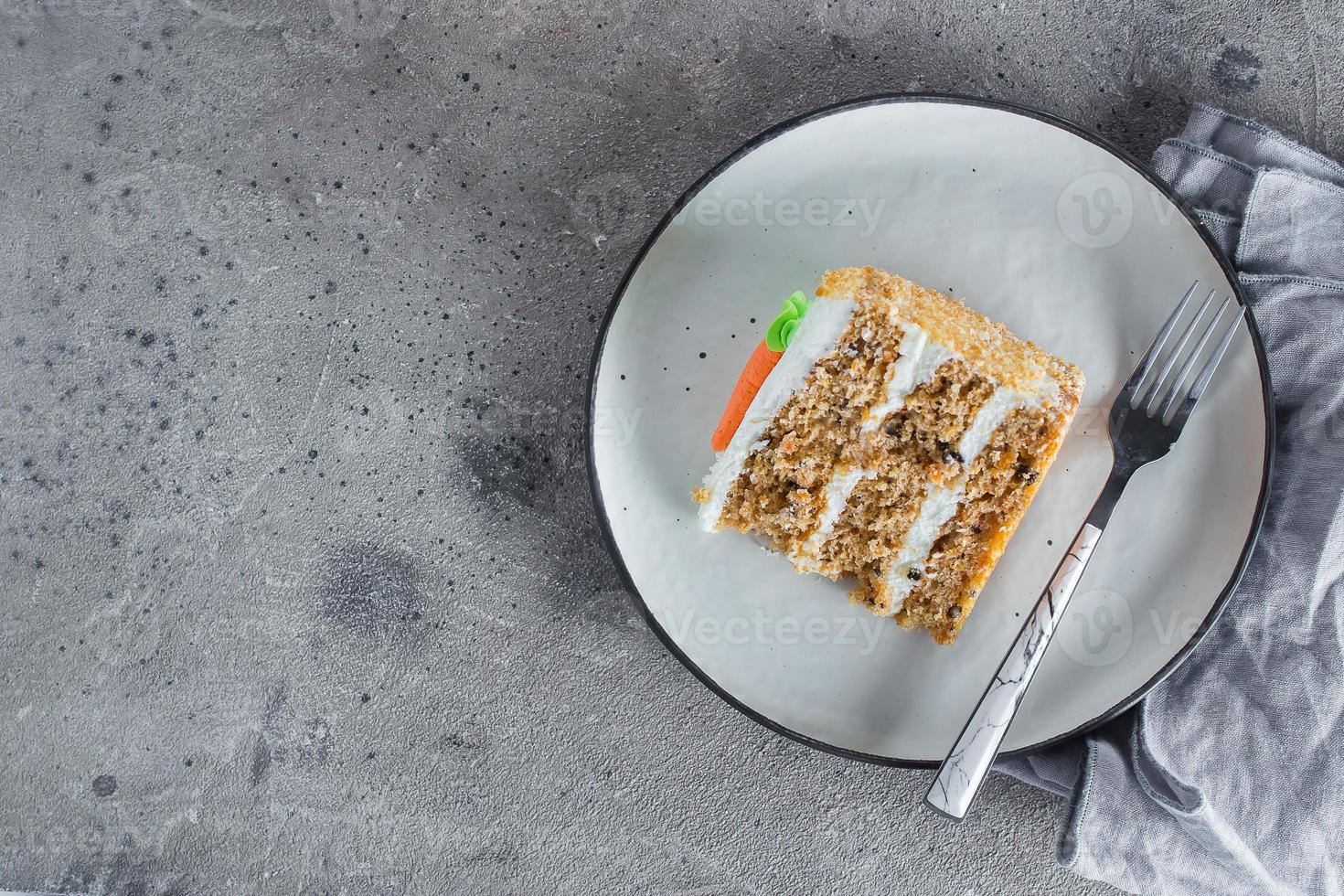 Slice of homemade carrot cake with cream cheese frosting on plate on gray stone table background photo
