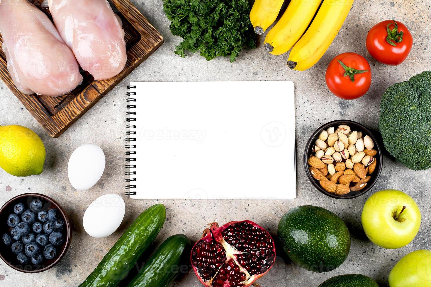 Keto diet food concept. chicken fillet, eggs, green vegetables, tomatoes, nuts and fruits on light concrete table background. Flat lay, top view, copy space. Mockup concpt with empty white notebook. photo