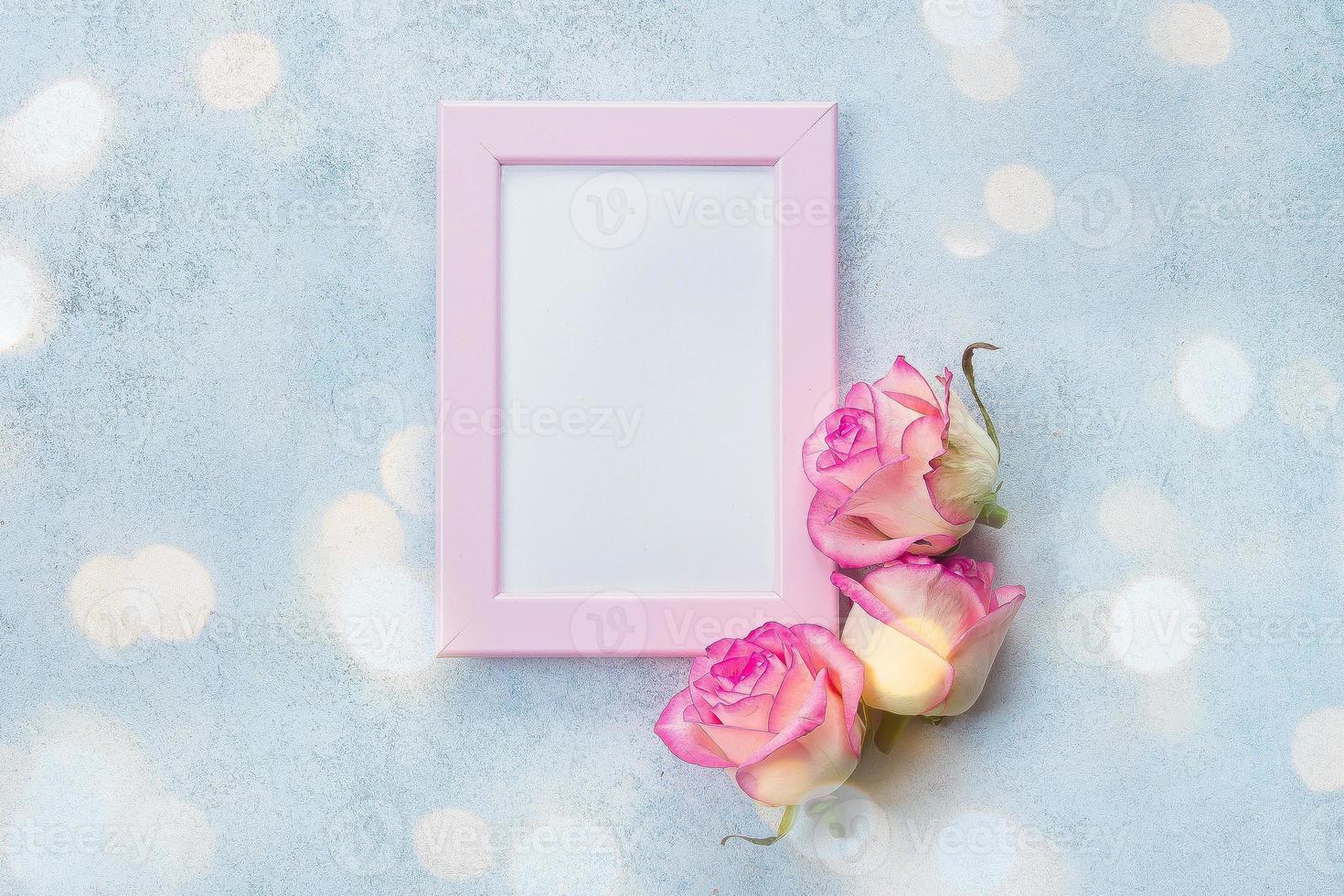 Holiday card concept. Photo frame with place for text and pink roses on blue background. Top view, flat lay. Mock up