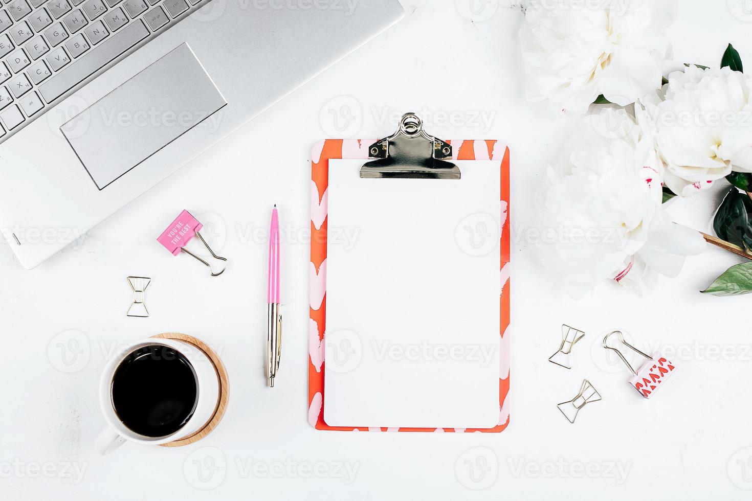 Workplace with laptop, cup of coffee, flowers peonies, pen, clipboard. Flat lay, top view, mockup photo