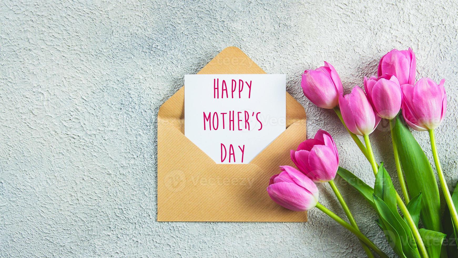 tarjeta del día de la madre. flores de tulipanes rosas y tarjeta con texto sobre fondo de hormigón. endecha plana, vista superior. bandera foto