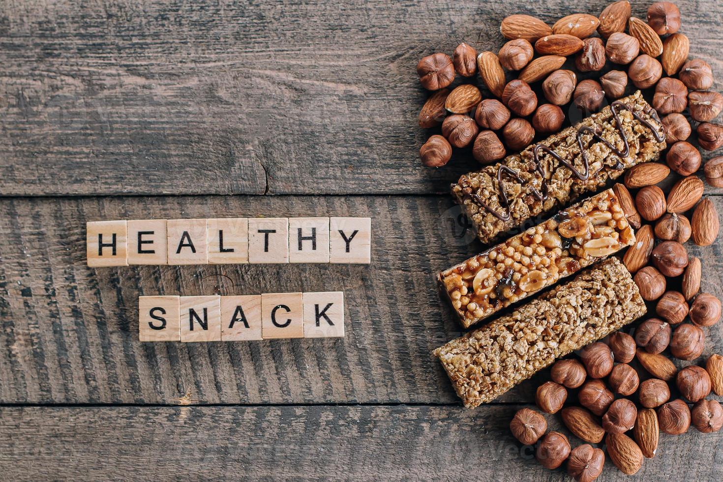 Cereal Granola bars and almond, hazelnut nuts. Old Brown Wooden Table Background. Wooden letters words text Healthy Snack Bars. Top view photo