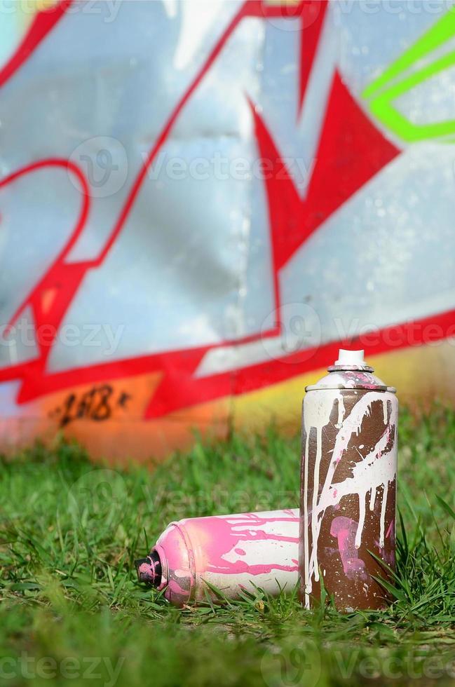 unas pocas latas de pintura usadas yacen en el suelo cerca de la pared con una hermosa pintura de graffiti. concepto de arte callejero y vandalismo foto