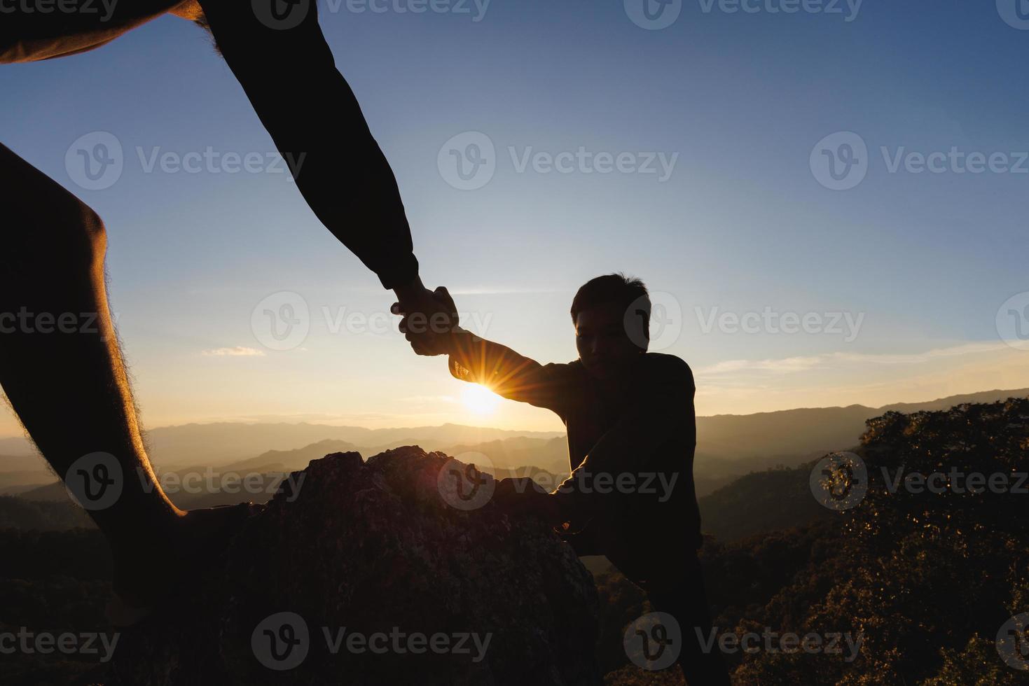 Hikers climbing up mountain cliff and one of them giving helping hand. People helping and, team work concept. photo