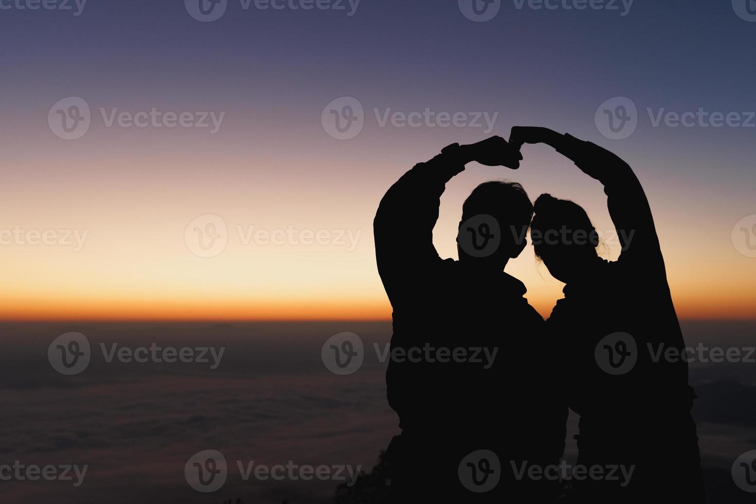 Silhouette  of the romantic scene of the couple sitting on the hill at sunset time. young couple tenderly embracing in the sunset. photo