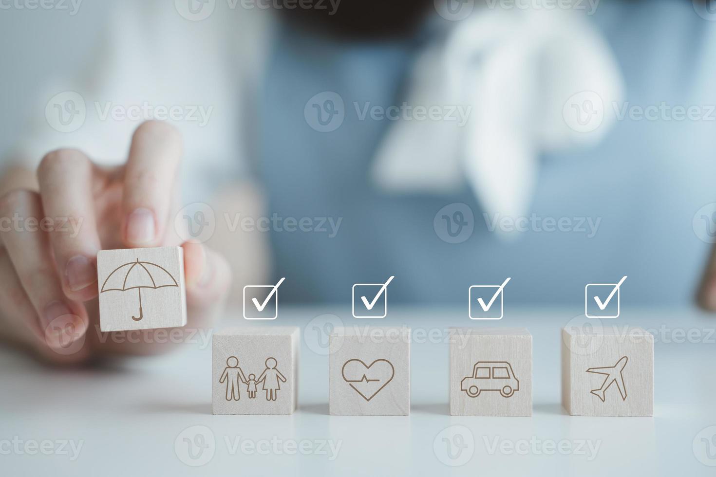 Insurance concept. Protection against a possible eventuality. Hand holding umbrella icon for security symbol and car, family, travel and health on wooden block with check mark. Life assurance concept. photo