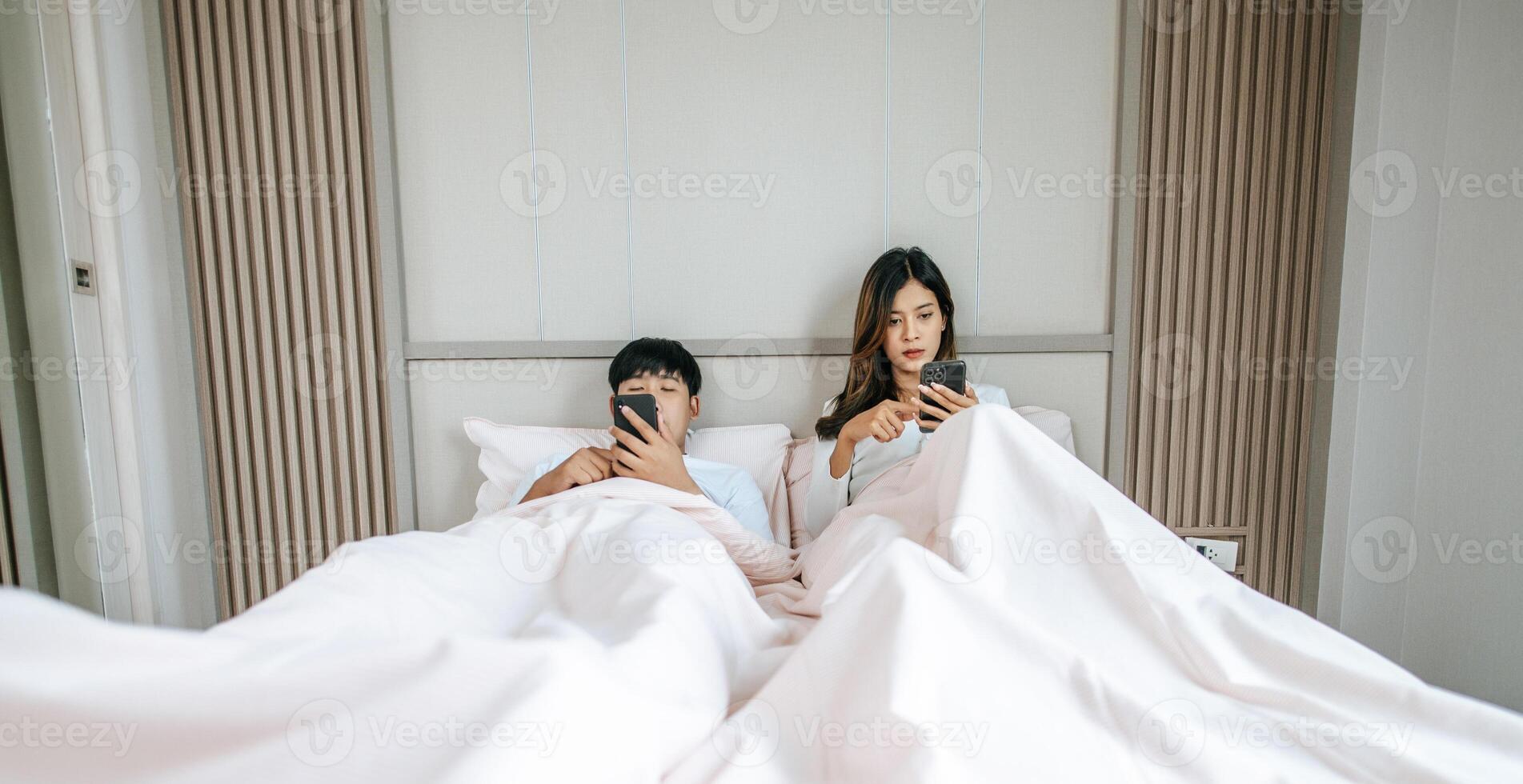 Young Couple lying on bed with smartphone ignoring each other photo